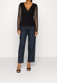 Black lace long-sleeve top with a V-neck design, paired with dark denim straight-leg jeans and open-toed black heels.