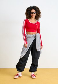 Röd croppad långärmad topp med vit kant och tre vita ränder, grå sweatshirt liggande, svarta baggy-byxor och flerfärgade sneakers.