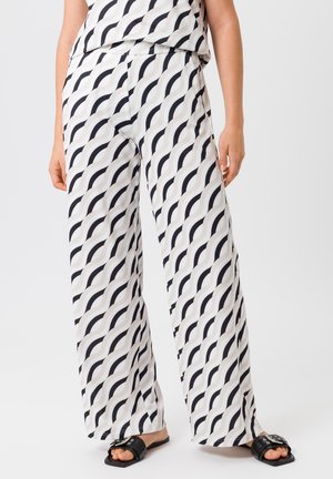 Pantalons larges blancs avec un motif ondulé en noir et gris. Tissu léger avec une texture lisse, associés à des sandales noires simples.