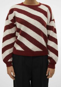 Maglione a righe rosse e crema con scollatura rotonda, maniche lunghe e polsini a costine. Tessuto morbido e strutturato. Abbinato a pantaloni neri.