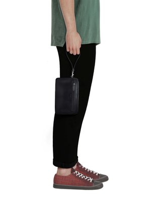 Person wearing black pants and red sneakers holds a small black zippered pouch by its wrist strap at their side.