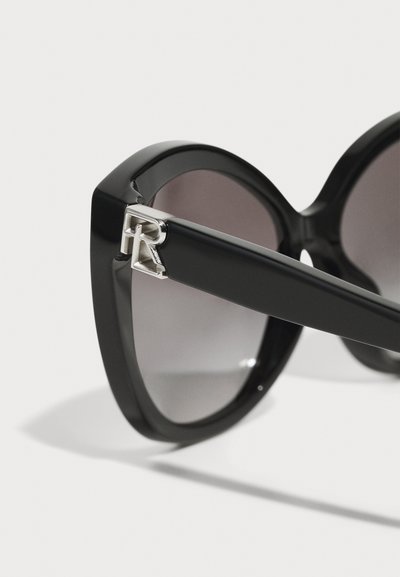 Black oversized sunglasses with a glossy frame, gradient lenses, and a silver accent depicting an "R" on the side.