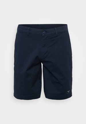 Pantaloni corte blu navy in tessuto di cotone, dotati di chiusura con bottone, passanti per cintura e una piccola etichetta logo sul lato sinistro.