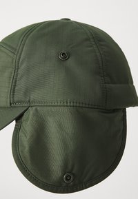 Gr�øn stofkasket med et struktureret design, der har en blød skygge og mesh-detaljer. Bemærkelsesværdig for sit teksturerede, gitterlignende mønster og trykknaplukning.