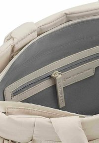 Intérieur d'un sac en tissu beige, avec une doublure grise et un compartiment zippé avec un tirette de marque. Texture lisse, agencement design organisé.