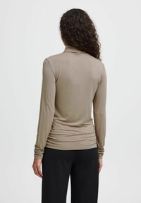 Top beige de manga larga con cuello alto, que presenta un diseño ajustado y tejido fruncido en la cintura. Textura suave, combinado con pantalones negros.