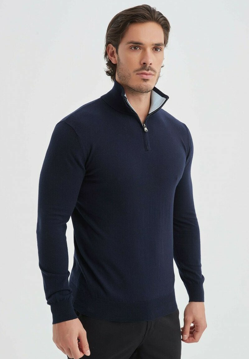 Un sweat à fermeture éclair bleu marine en tissu lisse et texturé. Il présente des manches longues, un col montant avec une doublure intérieure contrastante, et des poignets côtelés.