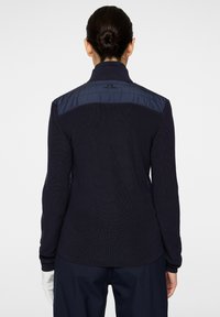 Marinblå tröja med strukturerad stickad kropp och slät, vadderad övre del av ryggen. Har en hög krage och långa ärmar, designad för värme och komfort.