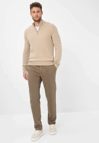 Maglione beige a maglia con colletto a zip, abbinato a chinos marrone chiaro e sneakers bianche. Tessuto morbido e design aderente.