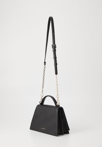 Czarna skórzana torebka o wyraźnym kształcie, ze składanym projektem, górną rączką i odpinanym łańcuszkiem. Złote akcenty.
