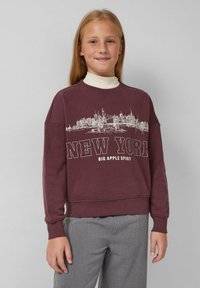 Felpa bordeaux con collo a giro, caratterizzata da una grafica della skyline bianca e il testo "NEW YORK". Abbinata a pantaloni grigi, su uno sfondo neutro.