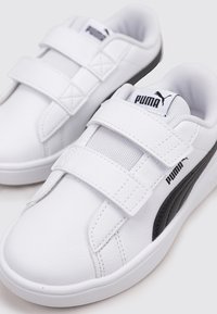 Scarpe sintetiche bianche con due cinturini in velcro, accenti neri sui lati e una linguetta testurizzata con il logo Puma.