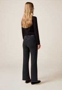 Sorte, vidde bukser med frynset kant og baglommer, kombineret med en sort, langærmet top, set bagfra. Glat stoftekstur.