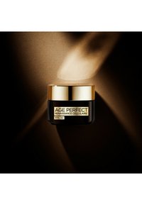 Pot noir avec accents dorés, étiqueté "AGE PERFECT RENAISSANCE CELLULAIRE FPS 30." Surface lisse, forme circulaire compacte, posé sur un fond sombre.