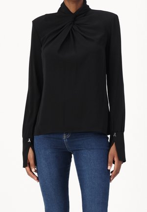 Zwarte blouse met een hoge hals en gedraaide voorkant. Heeft lange mouwen met manchetopeningen en subtiele metalen accenten.