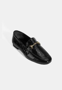 Zwarte patenten leren loafers met een gestructureerd krokodillenpatroon, voorzien van een gouden kettingaccent op de wreef en een platte zool.