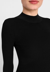 Top lungo a maniche nere a costine con collo alto, caratterizzato da un design aderente e una texture morbida, che mette in risalto linee verticali e una finitura senza cuciture.