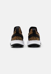 Sneaker con tomaia nera e stampa leopardata, cinturini elastici e intersuola bianca. Dettagli testurizzati sul tallone e suola esterna liscia nera.