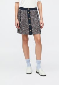 Tvidu mini svārki ar daudzkrāsainu faktūras rakstu, ar tumši zilu jostasvietu un zelta pogām priekšpusē.