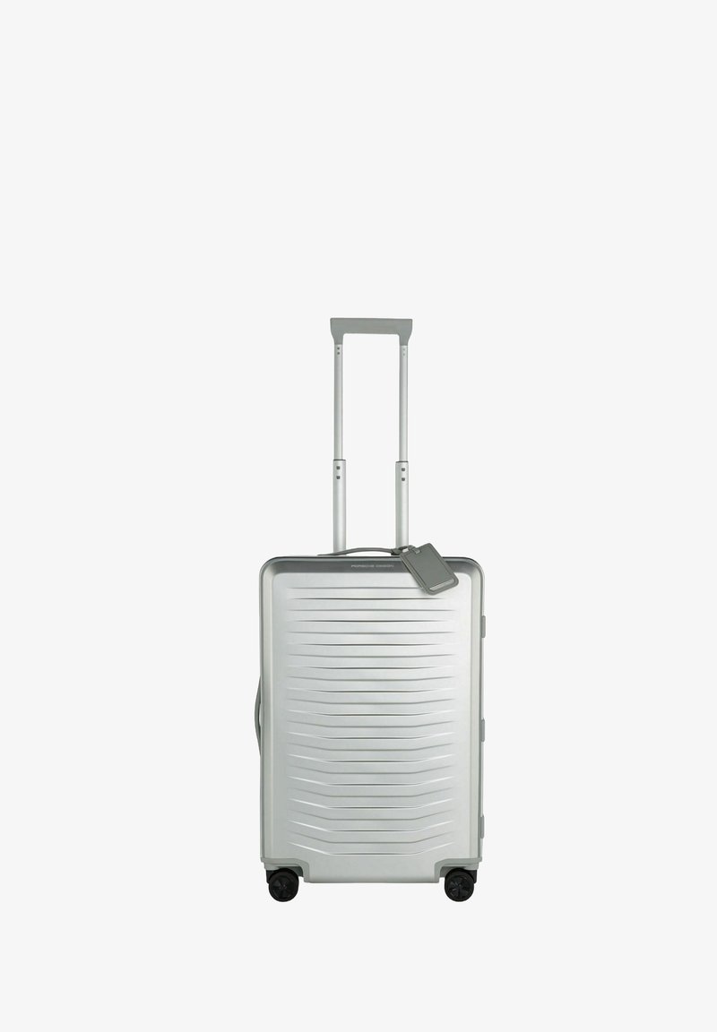 Valise rigide argentée avec un design texturé et linéaire, poignée rétractable et quatre roues. Comprend une étiquette de bagage détachable.