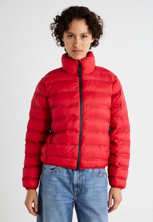 Rød pufferjakke med høy krage, quiltet design, frontglidelås og sorte detaljer. Brukt med denimjeans som har en avslappet passform.