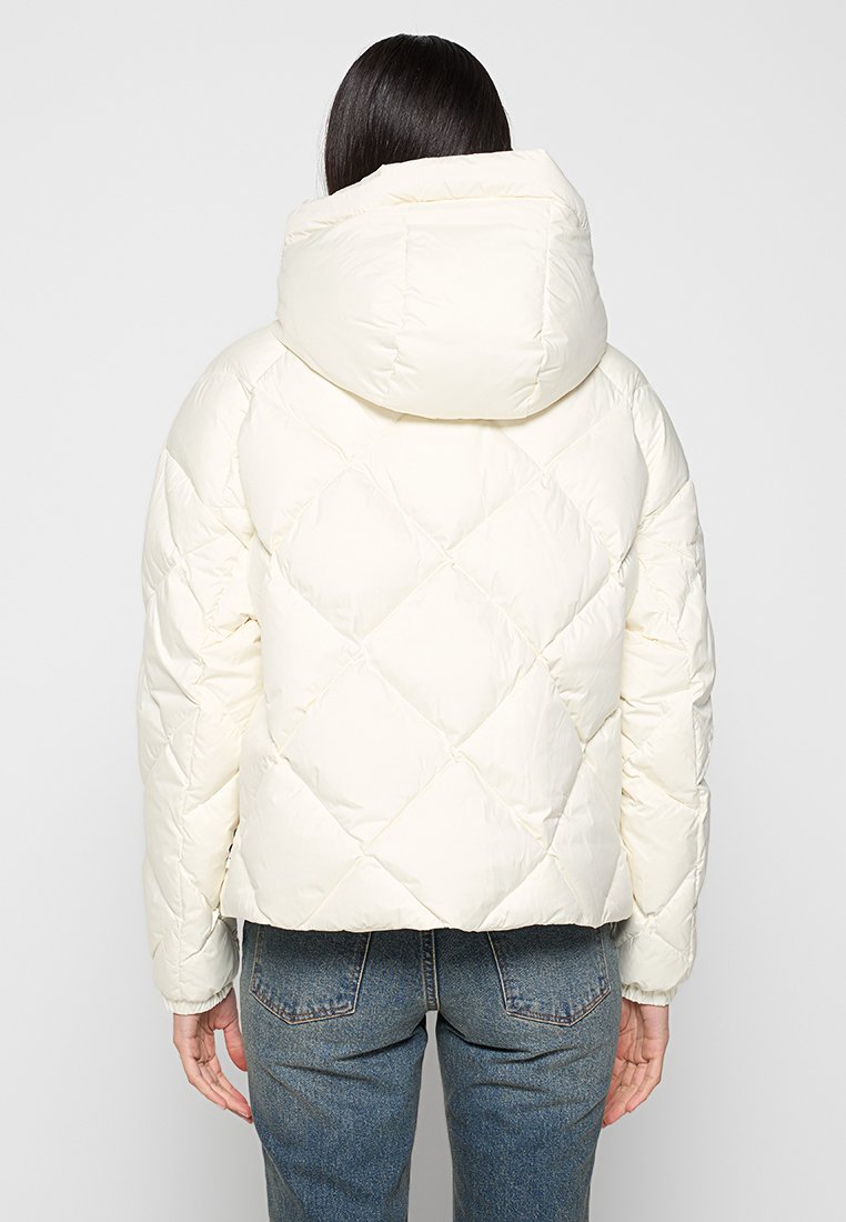 Gevoerde witte jas met een diamantvormig quiltpatroon en een grote, ronde kap. Zachte textuur, cropped ontwerp en aansluitende mouwen.