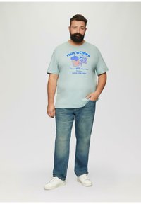 Jasnoniebieska koszulka z grafiką i napisem "FISH 'n CHIPS", w połączeniu ze średnio niebieskimi dżinsami i białymi trampkami. Prosty design i swobodny styl.