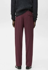 Pantalones plisados color granate hechos de tela suave, con un bolsillo trasero con botón y corte recto en las piernas. Estilizados con un suéter de punto oscuro.