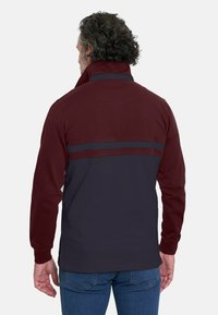 Chaqueta de hombre con una sección superior en burdeos y una sección inferior en azul marino oscuro, con franjas horizontales en contraste y un diseño de cuello alto.