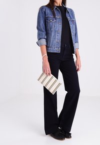 Džínová bunda světle modrého odstínu, černý top, černé vysokým pasem rozšířené kalhoty, černé mokasíny a pruhovaná psaníčko.