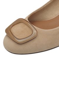 Chaussure plate en daim beige avec un grand détail de boucle carrée brillante sur l\'avant et une semelle intérieure marron rembourrée.