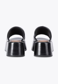 Sandales plateforme en cuir noir avec un dos ouvert et des lanières larges. Présente un talon épais et angulaire pour la stabilité et une silhouette unique.