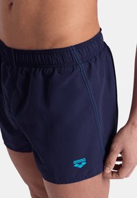 Costumi da bagno blu navy realizzati in materiale leggero con vita elastica, caratterizzati da cuciture blu e un logo acquamarina sulla gamba inferiore.