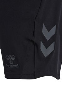 Section en tissu noir de shorts de sport avec deux bandes chevrons grises et un petit logo abeille Hummel gris près de l'ourlet.
