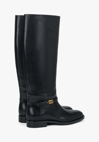 Czarne skórzane kozaki do kolan o gładkim wykończeniu, płaskich podeszwach i złotym detalu na pasku wokół kostki.