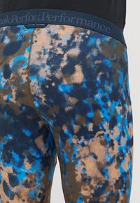 Leggings justas com um padrão multicolorido em azul, castanho e preto. Apresenta uma cintura elástica azul marinho com marcação e um detalhe de fecho.