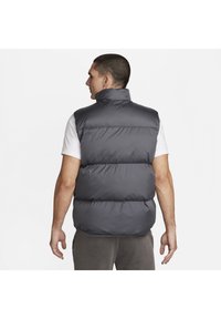 Gilet imbottito grigio con colletto alto, design trapuntato e vestibilità ampia, indossato sopra una maglietta bianca, che mette in evidenza una texture liscia e uno stile semplice.