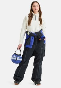 Conjunto de snowboard que incluye una parte superior crema, una chaqueta azul atada a la cintura, pantalones negros con costuras blancas y un casco azul con detalles.