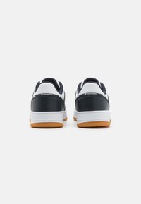Chaussures de sport pour hommes, en cuir bleu marine et empiècement synthétique blanc, col rembourré, semelle en caoutchouc avec accents orange, style bas.