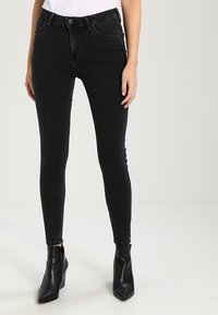 Jeans skinnies negros de denim, con un diseño clásico de cinco bolsillos, ajuste ceñido y cintura media, combinados con botas negras de tobillo.