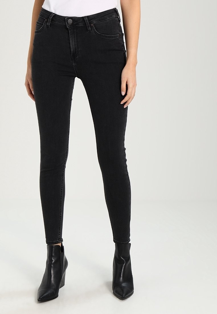 Jeans skinnies negros de denim, con un diseño clásico de cinco bolsillos, ajuste ceñido y cintura media, combinados con botas negras de tobillo.