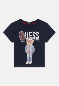 Marineblauwe katoenen t-shirt met een beerafbeelding in een spijkeroutfit, met rode accenten en de tekst "GUESS CALIFORNIA L.A. EST. 1981."