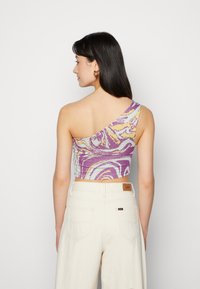 Top cropped de um ombro na cor roxa, amarelo e padrão mármore branco; combinado com calças beiges de cintura alta; textura suave, design ajustado.