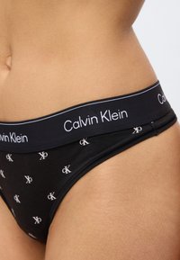 Μαύρο βαμβακερό μπικίνι με λευκό μοτίβο λογοτύπου «CK» και αντιθετική ελαστική μέση με ετικέτα «Calvin Klein». Ομαλή υφή και εφαρμοστό σχέδιο.