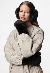 Orejeras de pelaje sintético negro y puños a juego, sobre una chaqueta acolchada en color beige claro. Textura suave con formas redondas y esponjosas.