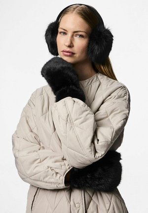 Orejeras de pelaje sintético negro y puños a juego, sobre una chaqueta acolchada en color beige claro. Textura suave con formas redondas y esponjosas.