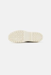 Suela de una zapatilla Converse blanca con patrones de tracción geométricos y el logo de Converse grabado en el centro.