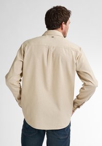Beige lange mouwen shirt met een rechte snit, voorzien van een rugplooi, knoopmanchetten en een kraag. De stof lijkt lichtgewicht en heeft een gestructureerde textuur.