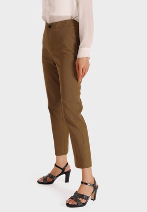 Pantaloni marroni a punta con una texture liscia, dotati di chiusura anteriore con bottone. Abbinati a sandali con tacco alto neri con decorazioni.