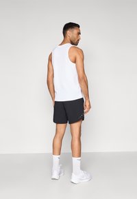 Άσπρο αμάνικο τοπ συνδυασμένο με μαύρο σορτς, παρουσιάζοντας έναν μονόχρωμο σχεδιασμό. Περιλαμβάνει άσπρες αθλητικές κάλτσες και άσπρα αθλητικά παπούτσια.